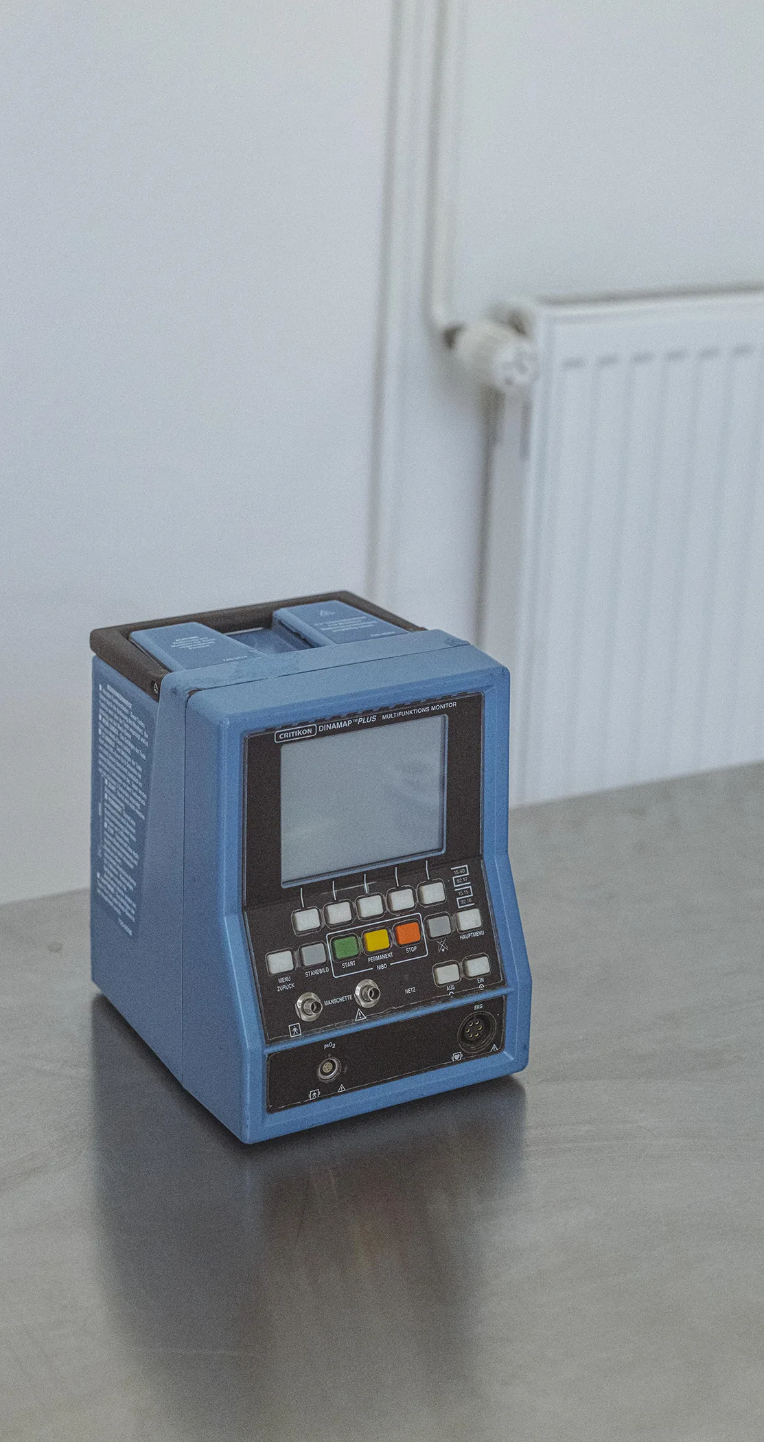 A blue electronic meter on a steel table by a white radiator