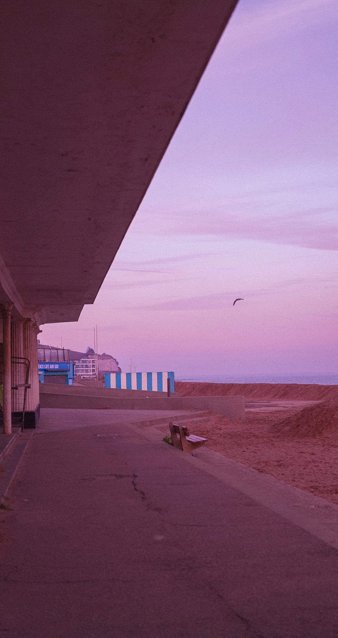 A shelter roof framing the promenade and beach huts under a violet sky, Margate