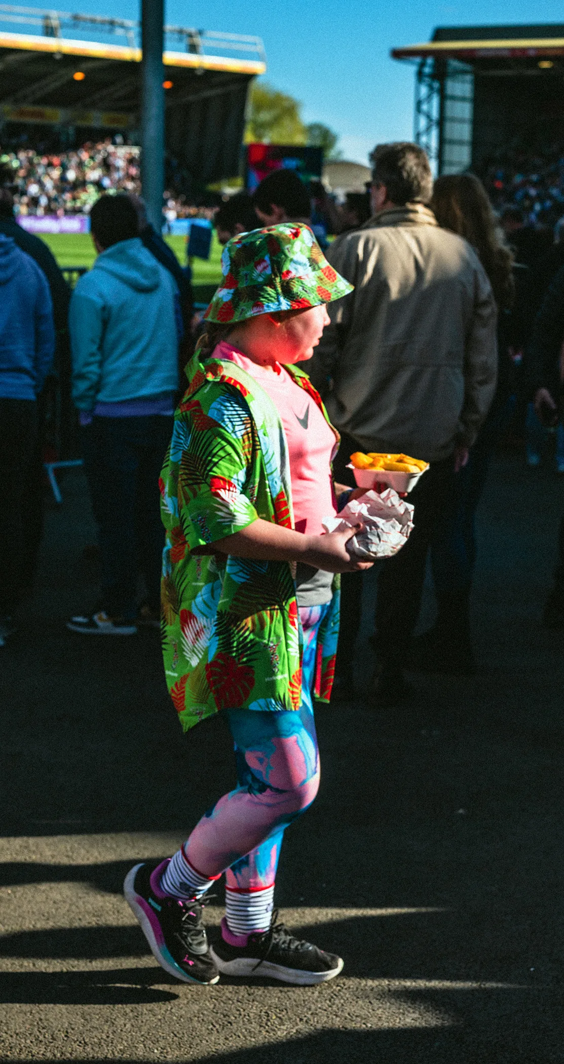 A fan in a bucket hat and floral shirt carrying chips along the concourse