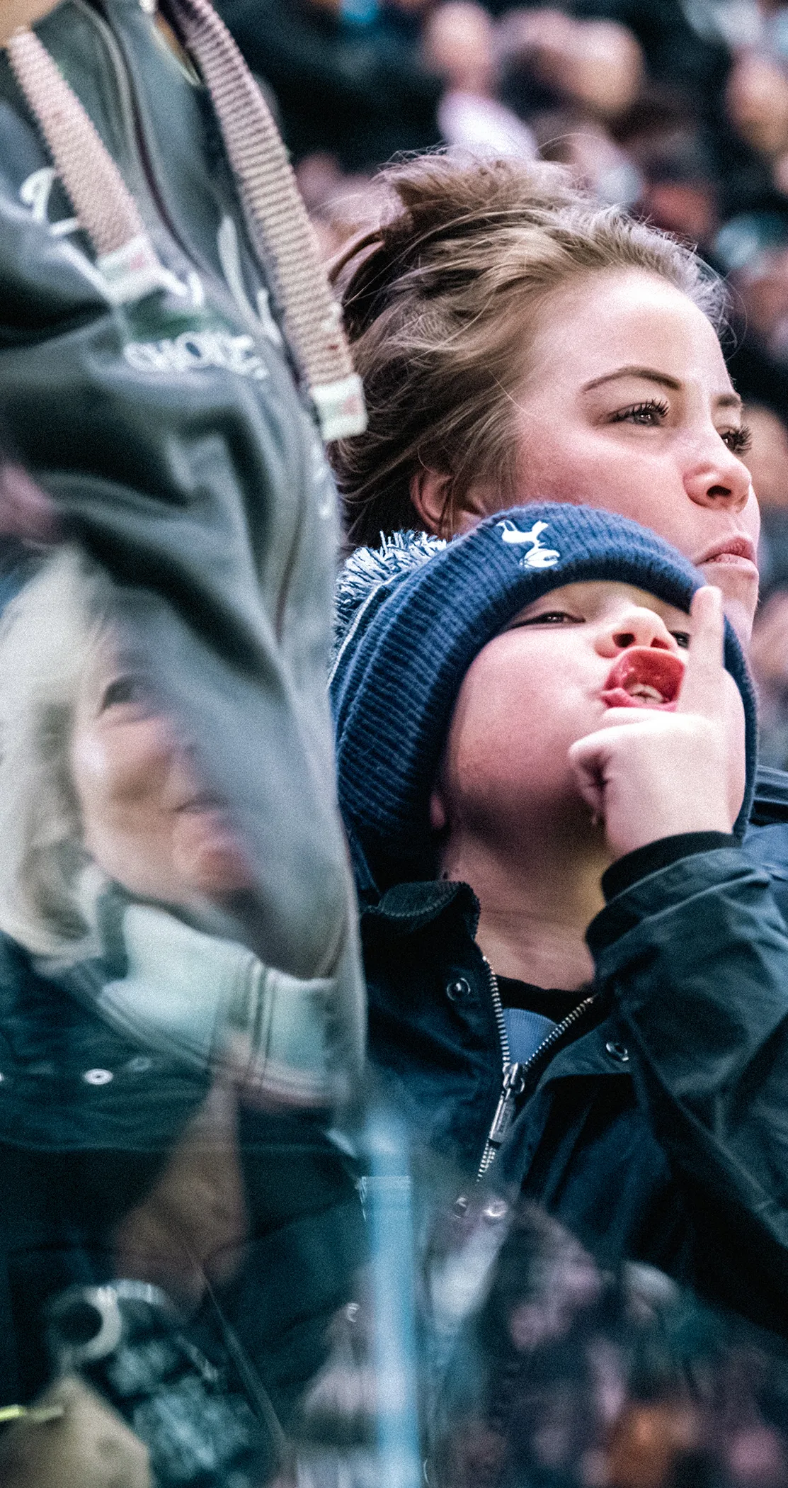 A young Spurs fan in a bobble hat watching with hand to chin among the crowd