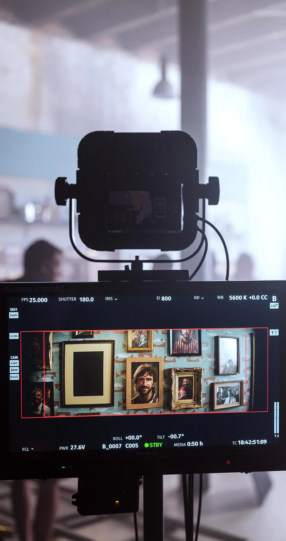 A camera monitor framing a wall of portraits, with a light rigged above