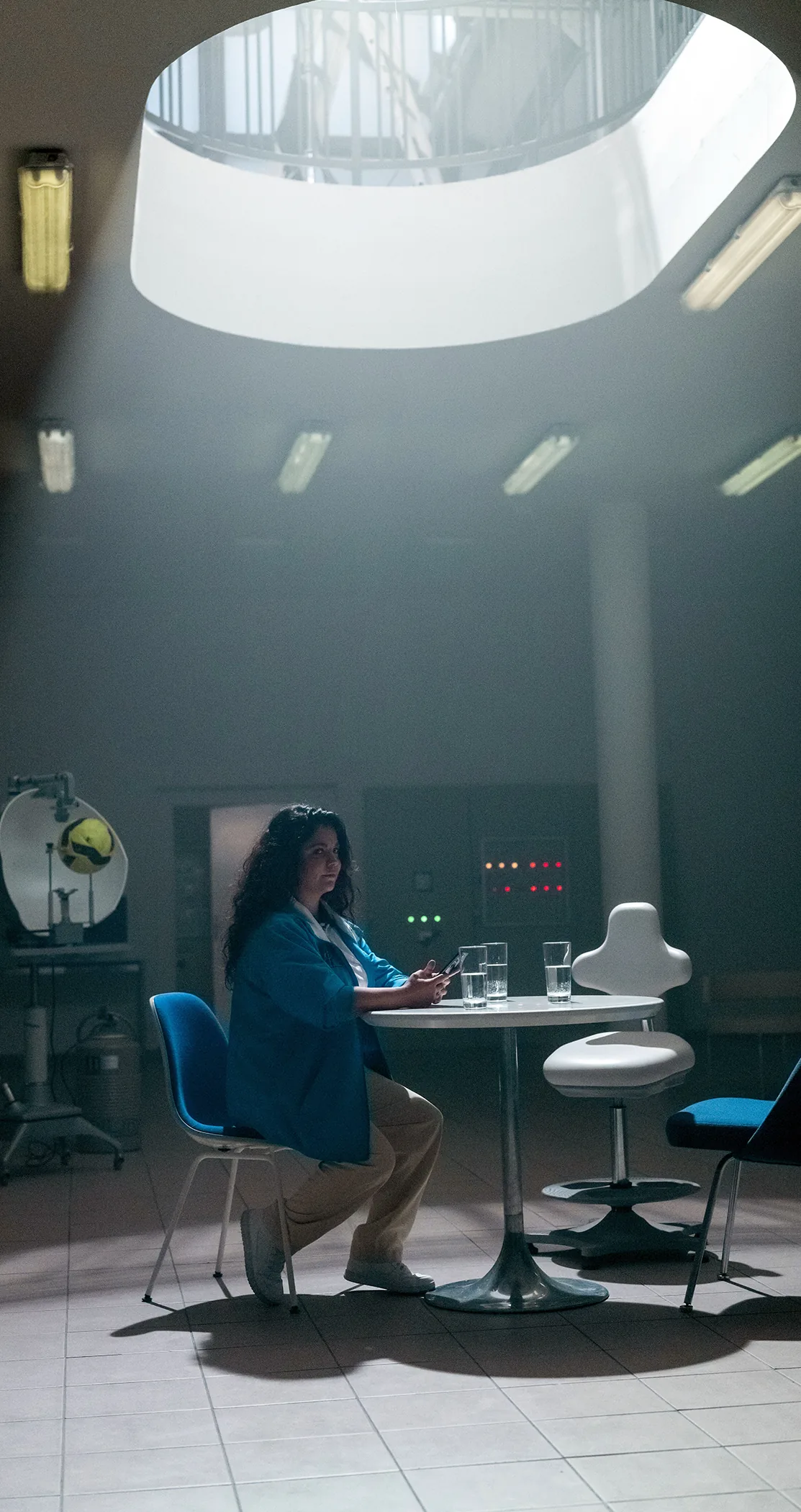 A woman at a round table beneath a skylight in a retro room