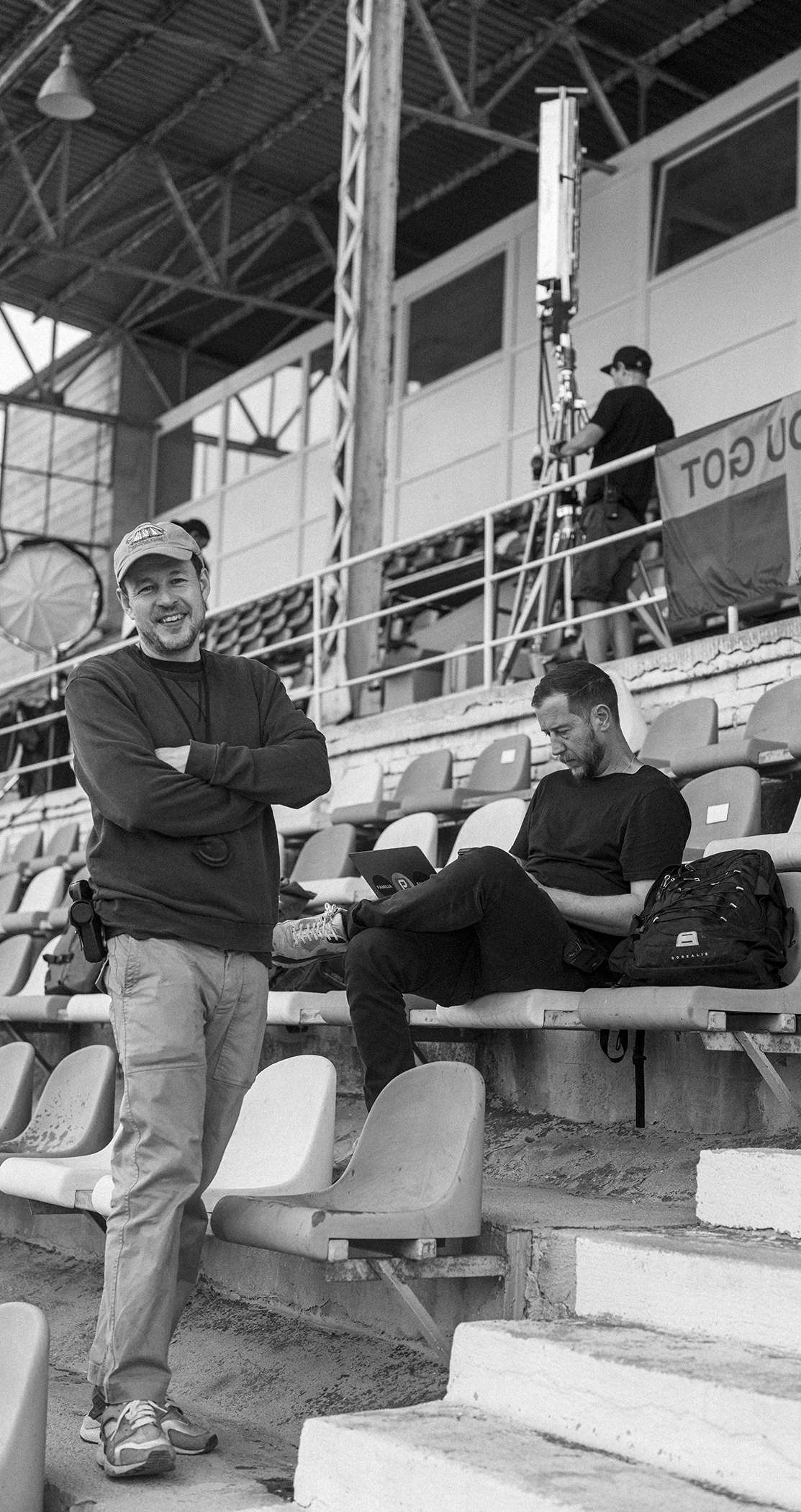 Two crew members resting in empty stadium seats, in black and white