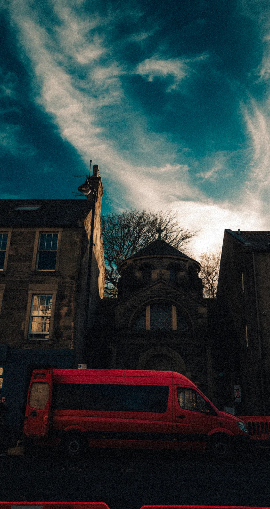 Sandstone buildings and an orange van in silhouette under a streaked sky