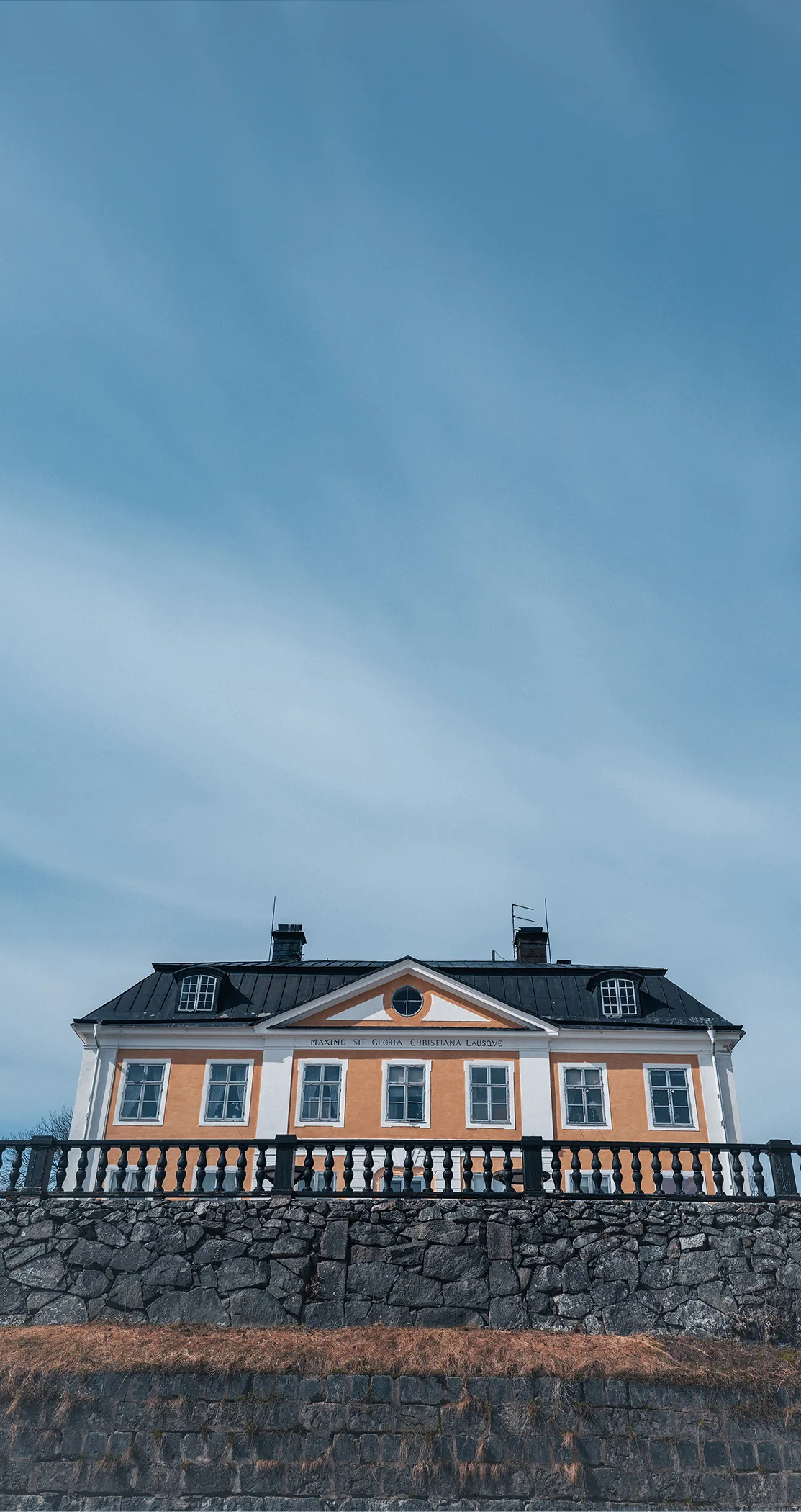 Yellow manor house above a stone wall under a wide sky, Sweden